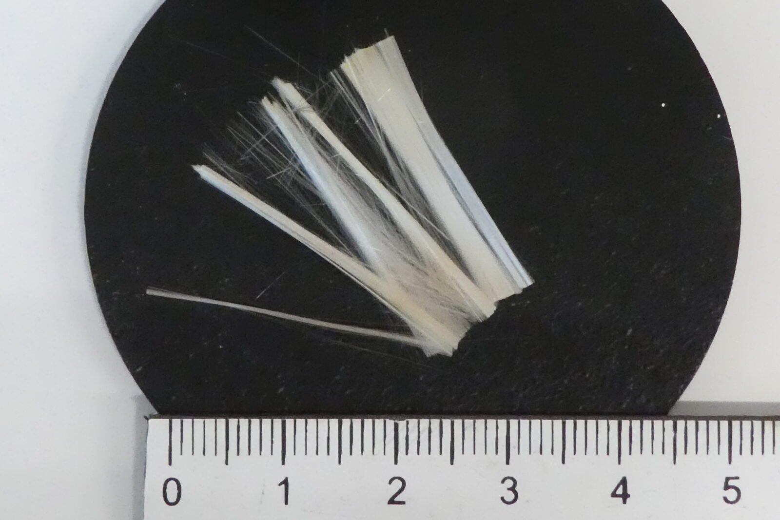 Recovered glass fiber bundle on matte black, next to a ruler — output of first pyrolysis trials